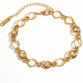 A gold-tone chain link bracelet with oval links and small clear stone accents, displayed on a clean white background. A brand tag is attached to one end of the chain.