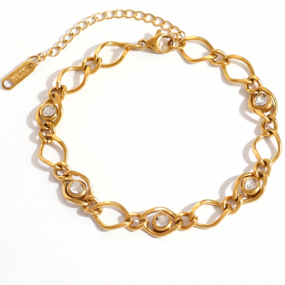 A gold-tone chain link bracelet with oval links and small clear stone accents, displayed on a clean white background. A brand tag is attached to one end of the chain.