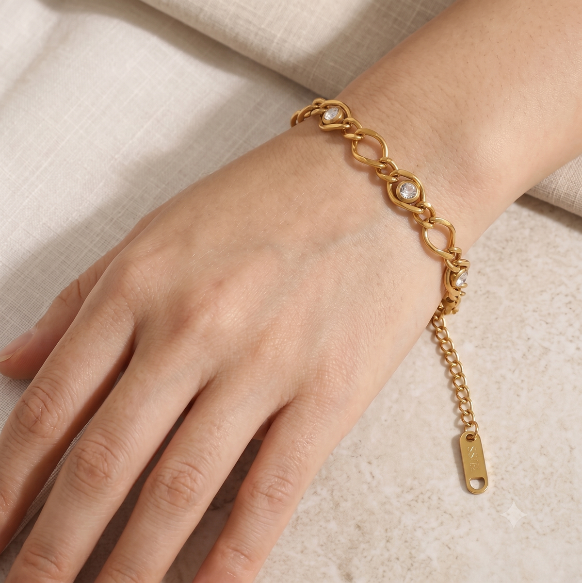 A gold chain bracelet with heart-shaped links and small clear stones, worn on a person's wrist. The bracelet includes an extender chain with a gold tag.